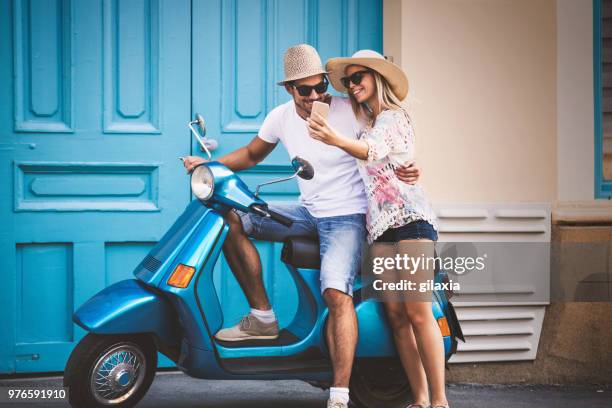 couple on a scooter bike driving through city streets. - women shorts stock pictures, royalty-free photos & images