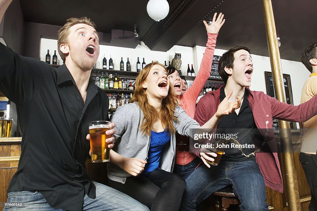 Cheering fans watch sport on television in pub bar