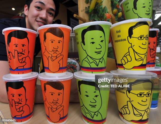 Warner Lee, spokesman for the furitjuice chain poses next to cups emblazoned with a portraits of Philippine presidential candidates former president...