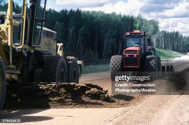 Forest road in northern Alberta is made up using a grader to level fill material followed on by a compactor unit hauled by a tractor - oilsands.