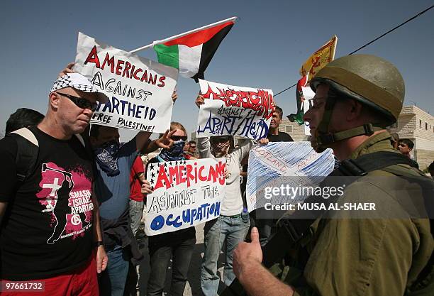 An Israeli soldier stands next to demonstrators during a protest against Israel's separation barrier in the West Bank village of Maasarah near the...