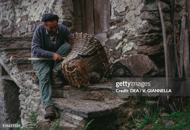 Farmer with his basket in front of a log cabin, Pecetto, Macugnaga, Anzasca valley, Piedmont, Italy.