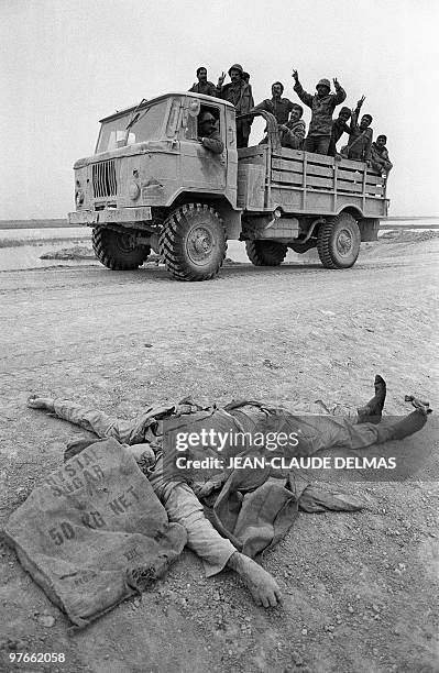 Iraqi troops flash V-signs as they move past a killed Iranian soldier on their way to the front line 18 March 1985 during the battle for the city of...