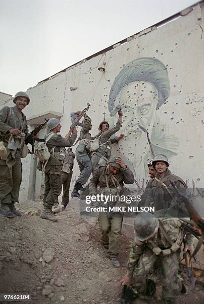 Iraqi soldiers pose 20 April 1988 in front of a huge bullet-pocked mural of Iranian leader Ayatollah Khomeiny in the strategic Faw peninsula of...