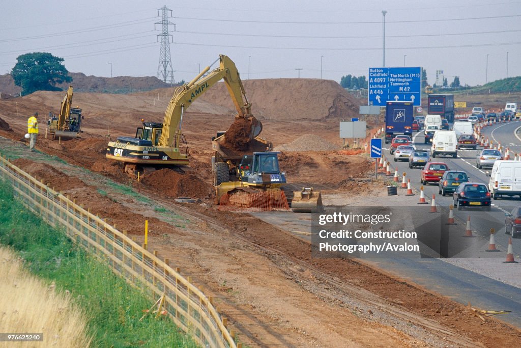 Caterpillar 330B crawler excavator working on slip road link from busy M42 motorway Junction 9 into the M6 Toll road.