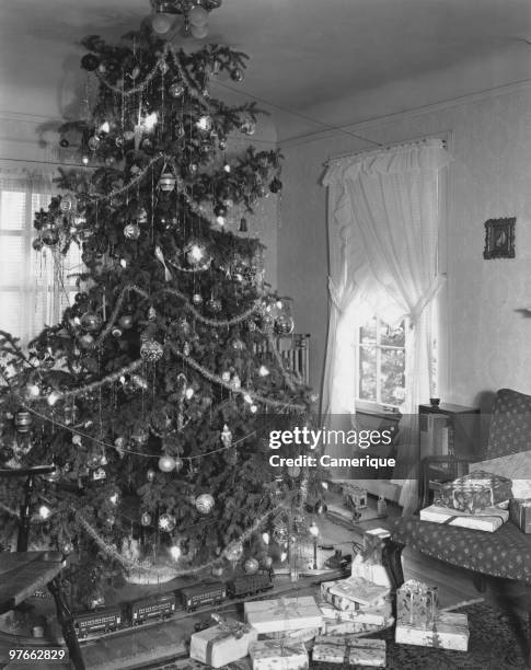 Train set and gift-wrapped presents under a large Christmas tree, circa 1955.