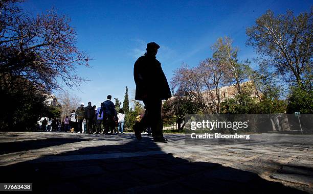 Pedestrians walk along the sidewalk under Acropolis hill in Athens, Greece, on Friday, March 12, 2010. European Union finance ministers will discuss...