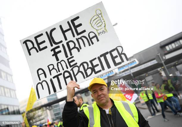 April 2018, Germany, Frankfurt/Main: Airport employees attend a rally at Frankfurt Airport. One of them holds up a sign reading 'Reiche Firma - arme...