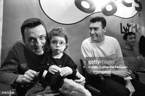 Young boy wearing glasses sits on the lap of Wiggle Murray Cook, while Greg Page looks on and smiles at an appearance by the children's music group...
