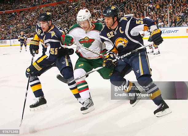 Jochen Hecht and Craig Rivet of the Buffalo Sabres battle for the puck with Nick Schultz of the Minnesota Wild on March 12, 2010 at HSBC Arena in...