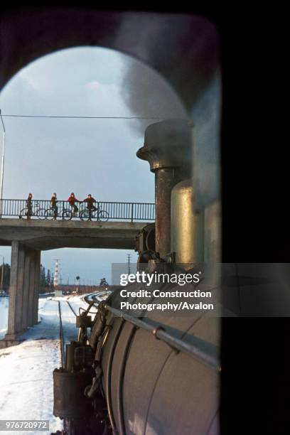 Four cyclists pause in their journey to admire the passing of Finnish Railway's TK3 Class No 1165 built by A/S Fricus in 1949. The engine was engaged...