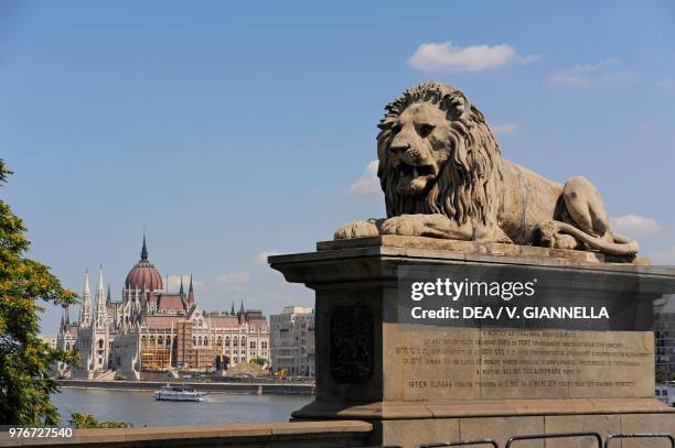 Stone lion at the entrance to the Chain Bridge, in the background the Parliament, Budapest, Hungary.