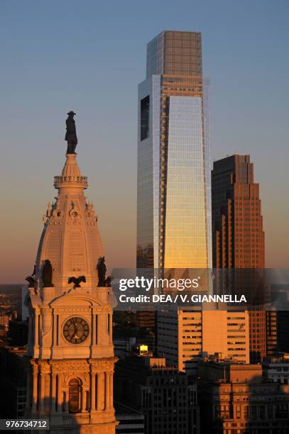 The tower of the town hall with the statue of William Penn, in the background skyscrapers at sunset, Philadelphia, Pennsylvania, United States of...