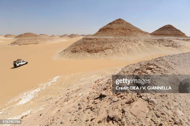 Rocky pyramids with an off-road vehicle on the left, Sahara desert, Egypt.