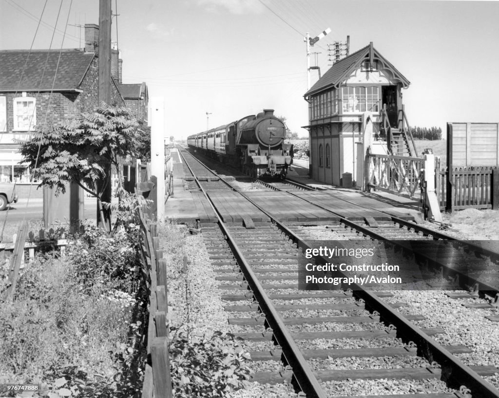 Thompson Class B1 at the head of a passenger train passes a signal box and level crossing at an unknown location in the east of England. C 1960