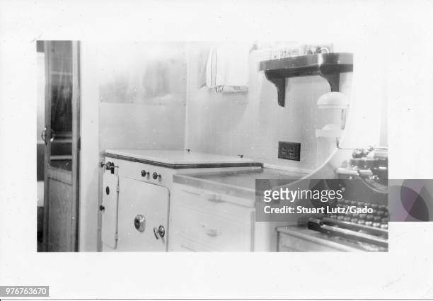 Black and white photograph, showing the cramped interior of a Mid-century caravan or trailer home, with part of a black typewriter visible next to a...