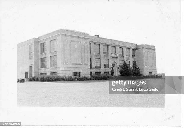 Black and white photograph, showing a slightly angled view of a large, flat-roofed, Art Deco building, with a brick facade, large rectangular...