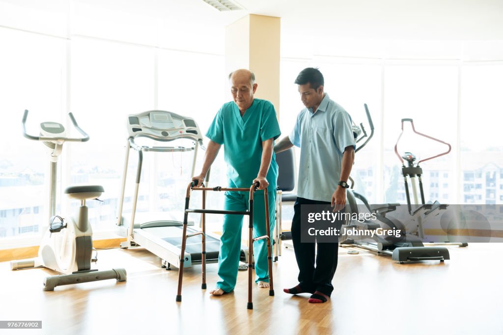Senior man using walking frame with physiotherapist helping