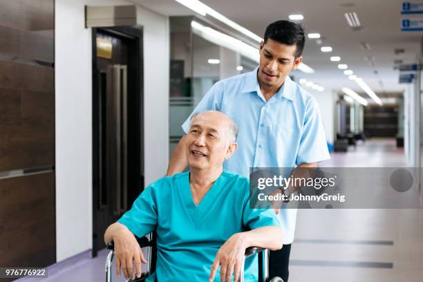 senior hombre empujada en silla de ruedas por enfermero - porter fotografías e imágenes de stock