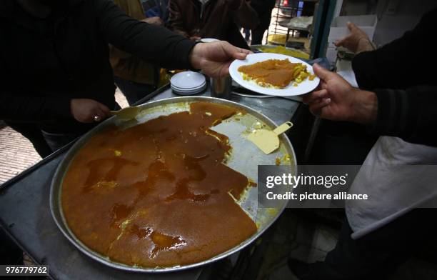 Palestinian man hands a plate of Kanafeh to a customer at Al-Aqsa sweets shop in the West Bank city of Nablus, 11 April 2018. Kanafeh, a traditional...