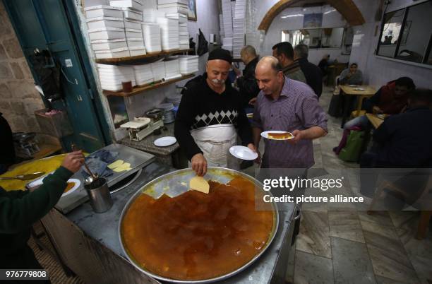 Palestinian man hands plates of Kanafeh to a customer at Al-Aqsa sweets shop in the West Bank city of Nablus, 11 April 2018. Kanafeh, a traditional...