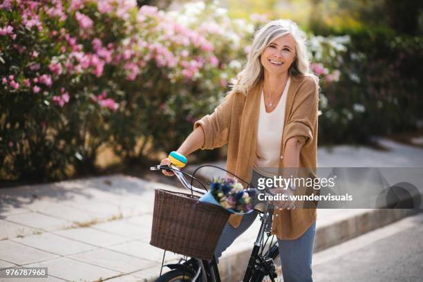 donna anziana sorridente che si diverte a guidare una bici d'epoca in primavera - primavera foto e immagini stock