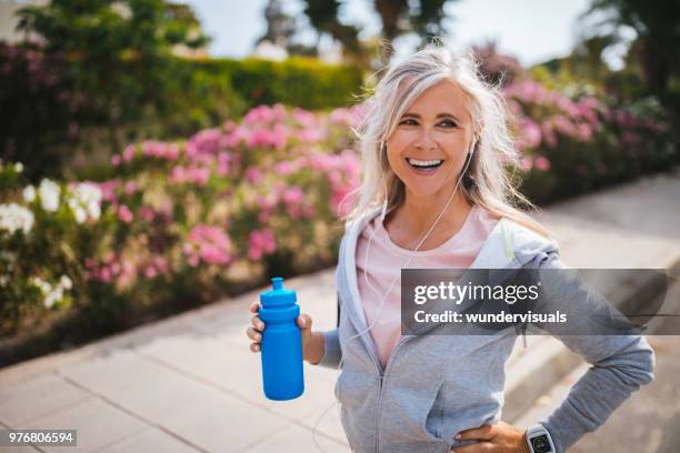 reife frau mit smartwatch mit wasser flasche während der bewegung in der natur - old woman running stock-fotos und bilder