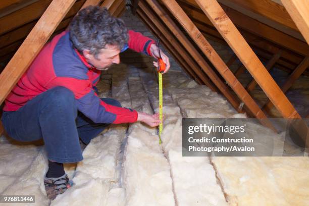 Man measuring the depth of insulation in a house loft or roof space Insulating your loft can save a significant amount of household heat loss and...