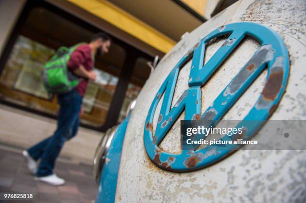 April 2018, Munich, Germany: A man walks past a Volkswagen Bulli of which the logo paint has pealed off. Photo: Lino Mirgeler/dpa