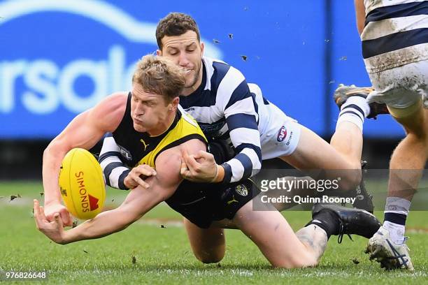 Josh Caddy of the Tigers handballs whilst being tackled by Sam Menegola of the Cats during the round 13 AFL match between the Geelong Cats and the...