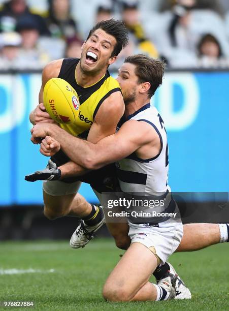 Alex Rance of the Tigers handballs whilst being tackled by Tom Hawkins of the Cats during the round 13 AFL match between the Geelong Cats and the...