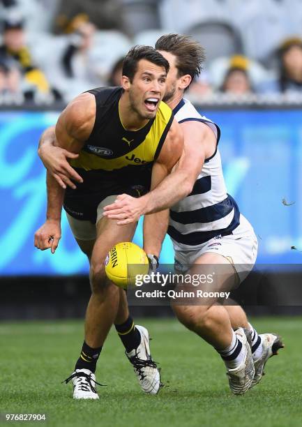 Alex Rance of the Tigers handballs whilst being tackled by Tom Hawkins of the Cats during the round 13 AFL match between the Geelong Cats and the...