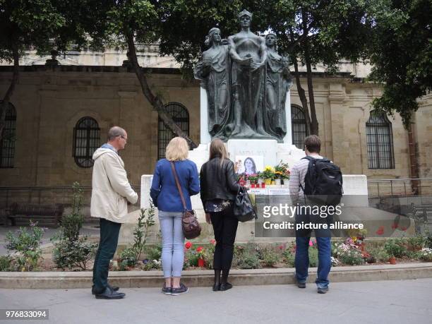 April 2018, Malta, Bidnija: Tourists in front of the improvised cenotaph of the murdered journalist Daphne Caruana Galizia lying at the feet of a...