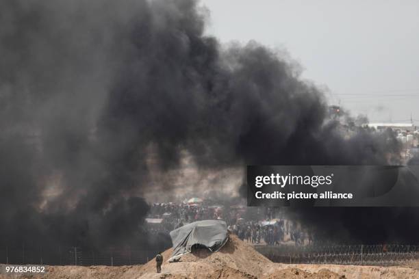 Dpatop - A picture taken from the Israeli side shows an Israeli soldier taking his position while columns of smoke rise after Palestinian protesters...