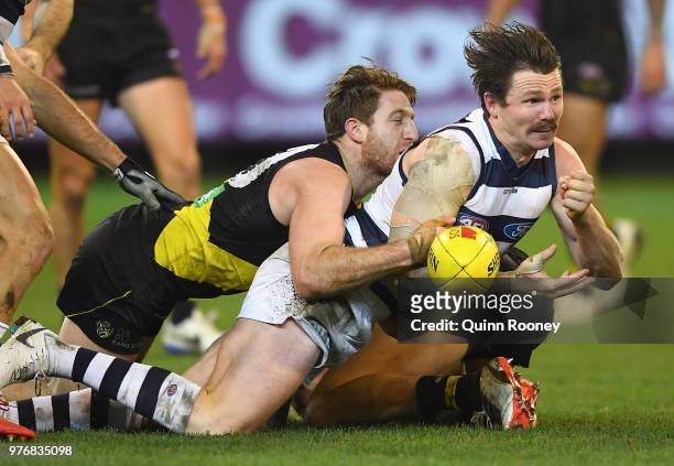 Patrick Dangerfield of the Cats handballs whilst being tackled by Reece Conca of the Tigers during the round 13 AFL match between the Geelong Cats...