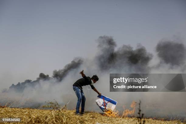 Dpatop - A Palestinian protester sets fire to an Israeli flag during clashes with Israeli security forces along the borders between Israel and Gaza...