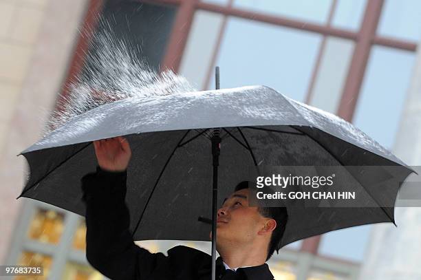 An usher flicks the snow off his umbrella during the closing session of the annual National People's Congress at the Great Hall of the People in...