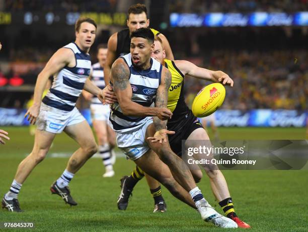 Tim Kelly of the Cats handballs whilst being tackled by Nick Vlastuin of the Tigers during the round 13 AFL match between the Geelong Cats and the...