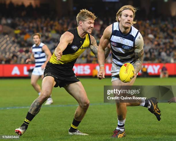 Tom Stewart of the Cats handballs whilst being tackled by Nathan Broad of the Tigers during the round 13 AFL match between the Geelong Cats and the...