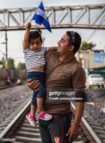 April 2018, Mexico, Mexico-City: A man carries a child on his arm who is holding the national flag of El Salvador in her hand as the wait for further...