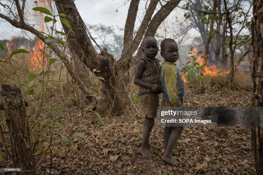 Two children stand in front of a fire their father lit to...