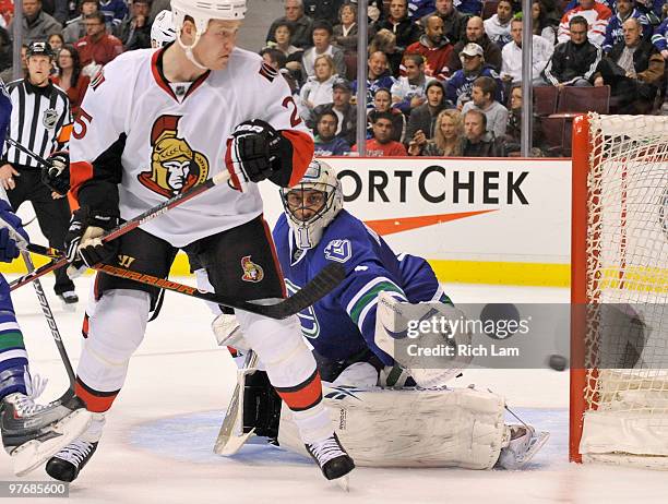 Goalie Roberto Luongo of the Vancouver Canucks watches the puck hit the post while Chris Neil of the Ottawa Senators fails to redirect it during the...