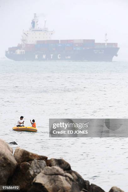 Man and boy paddle an inflatable dinghy after catching fish, as a container ship makes its way past Hong Kong's Aberdeen harbour on March 13, 2010....