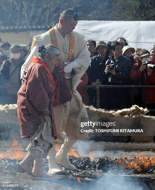 Buddhist ascentic monk leads an elderly lady as she walks barefoot through the flames during the "Hi-watari", or fire walking ceremony, to herald the...