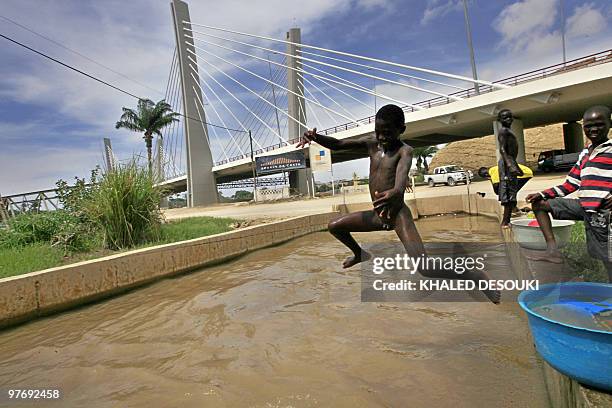 Naked Angolan boy jumps into a small canal from the Catumbla River under the newly constructed bridge in Lobito town about 25 km out of Benguela 500...