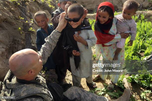 Army Chaplain Carl Subler puts his sunglasses on an Afghan boy while at an opium poppy farm on March 14, 2010 at Howz-e-Madad in Kandahar province,...