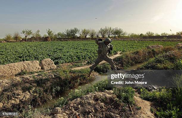 Army Chaplain Carl Subler jumps over an irrigation canal in an opium poppy field while on a military operation on March 14, 2010 at Howz-e-Madad in...