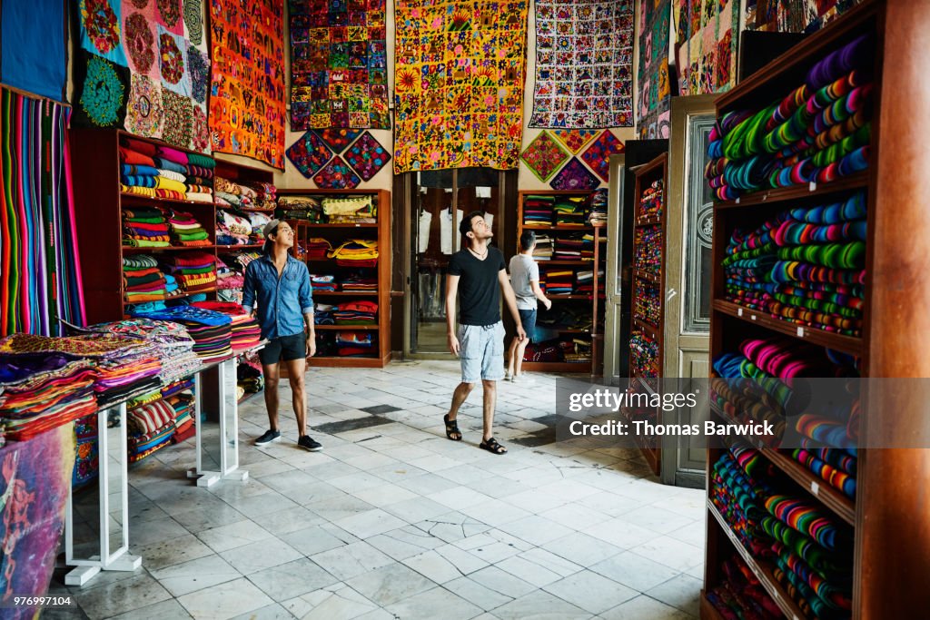 Three friends exploring local market filled with blankets and quilts