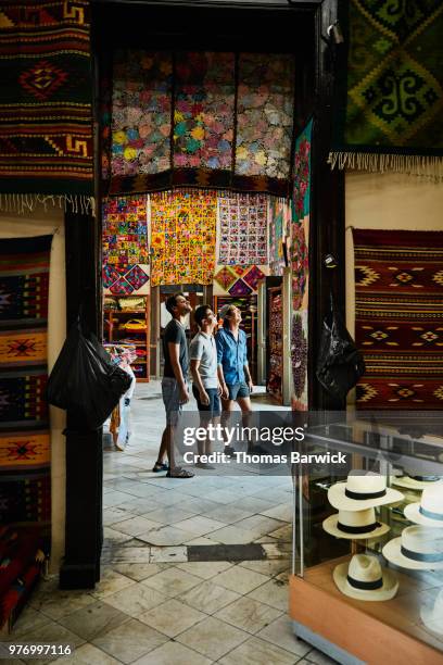 three friends looking at wall filled with blankets while shopping in local market - kulturpeis stock-fotos und bilder