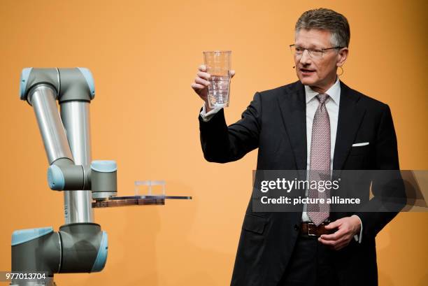 April 2018, Germany, Hannover: Elmar Degenhart, CEO of Continental AG, showing a glass half-filled with water next to a Cobot robot, which is to be...